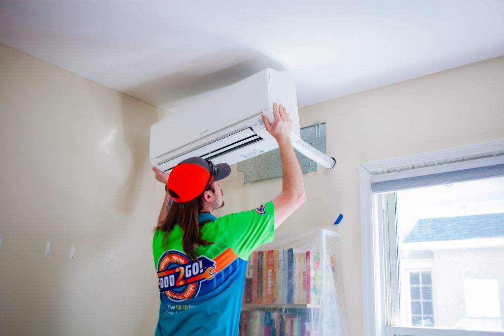 Good 2 Go technician installing a Mitsubishi mini-split unit near the ceiling