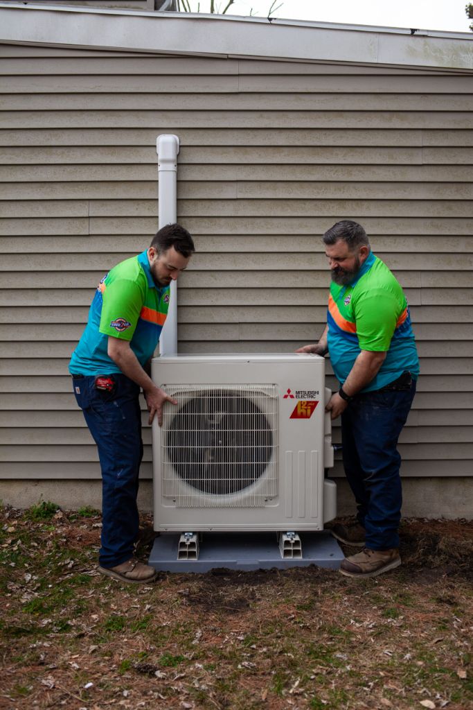 Two Good 2 Go technicians installing a Mitsubishi Electric outdoor heat pump unit